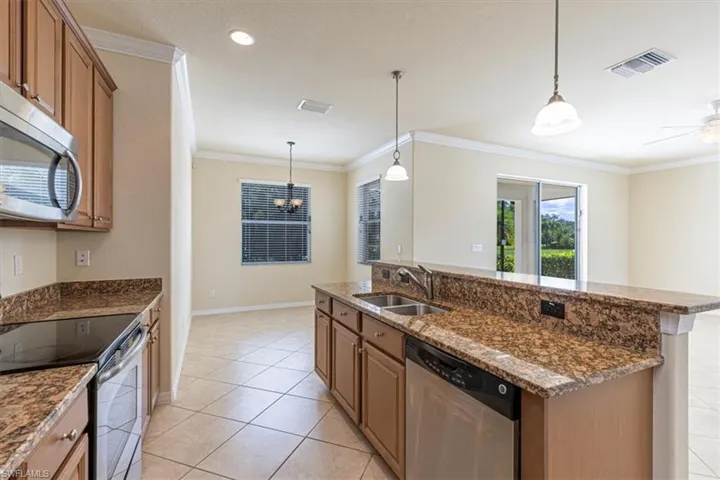 Kitchen featuring appliances with stainless steel finishes, ornamental molding, pendant lighting, brown cabinets, and light tile patterned floors