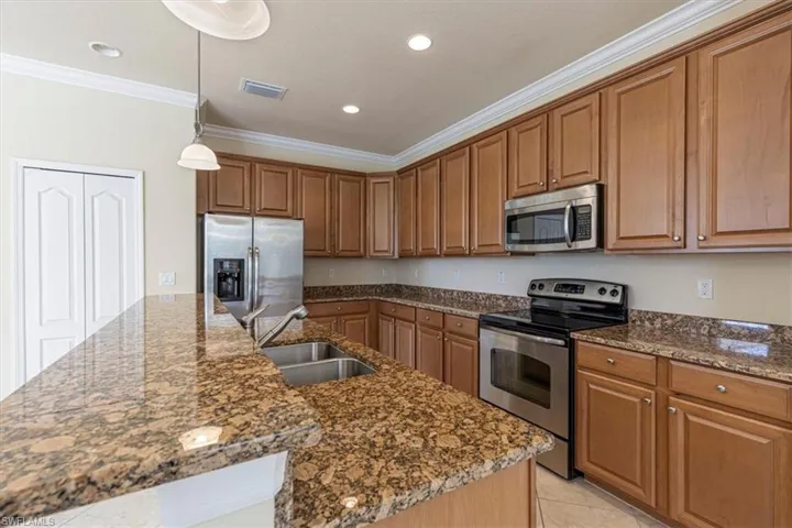 Kitchen featuring stainless steel appliances, hanging light fixtures, brown cabinets, crown molding, and light tile patterned floors