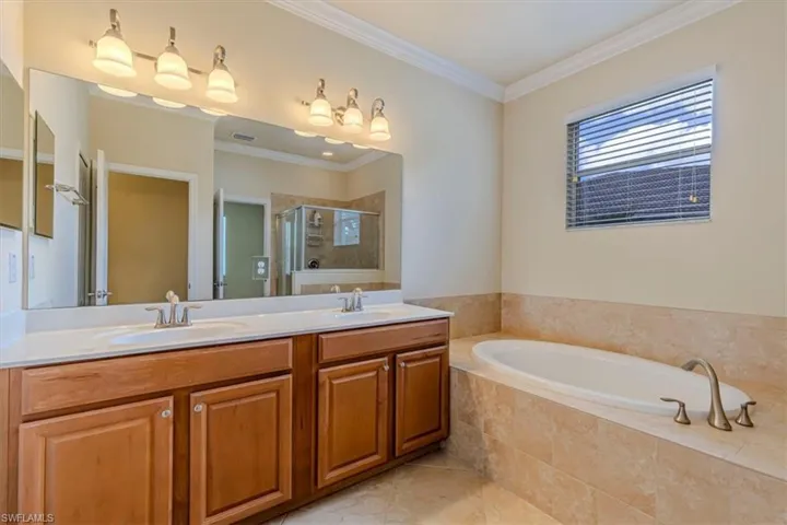 Full bath featuring ornamental molding, a shower stall, a bath, double vanity, and light tile patterned floors