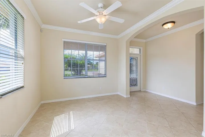 Spare room featuring crown molding, light tile patterned floors, arched walkways, and ceiling fan