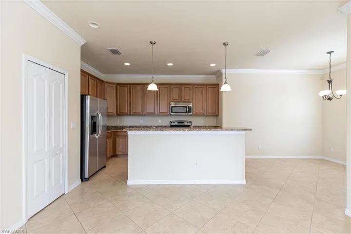 Kitchen featuring pendant lighting, stainless steel appliances, ornamental molding, a center island, and brown cabinets