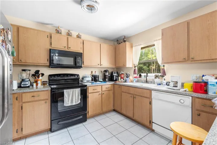 Kitchen featuring black appliances, a sink, light countertops, light tile patterned floors, and light brown cabinetry