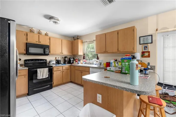 Kitchen featuring black appliances, a peninsula, light tile patterned floors, a sink, and a kitchen bar
