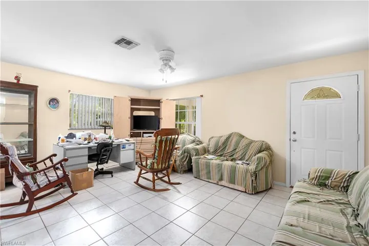 Living room with a ceiling fan, light tile patterned flooring, and a desk