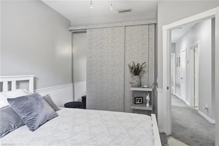 Bedroom featuring wainscoting, light gray walls, a contemporary closet system with sliding doors, a built-in shelving unit, and a carpeted hallway beyond