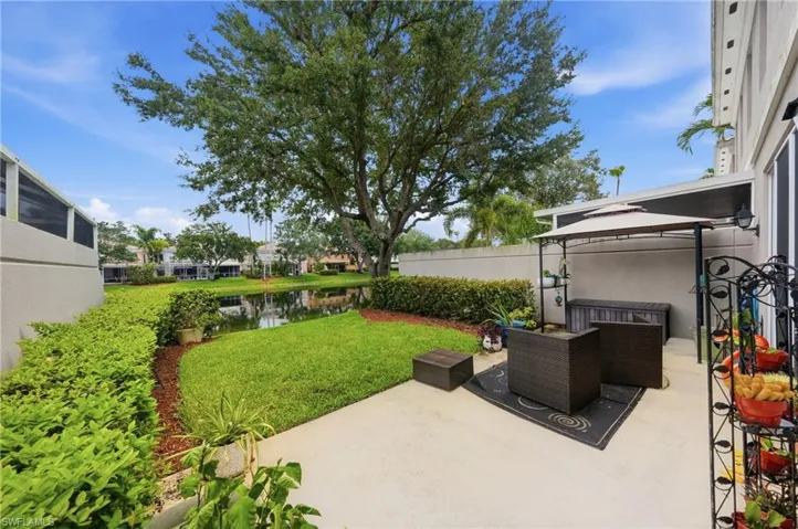 Paved patio area featuring a fixed white awning, outdoor lighting, and a manicured lawn bordering a water feature