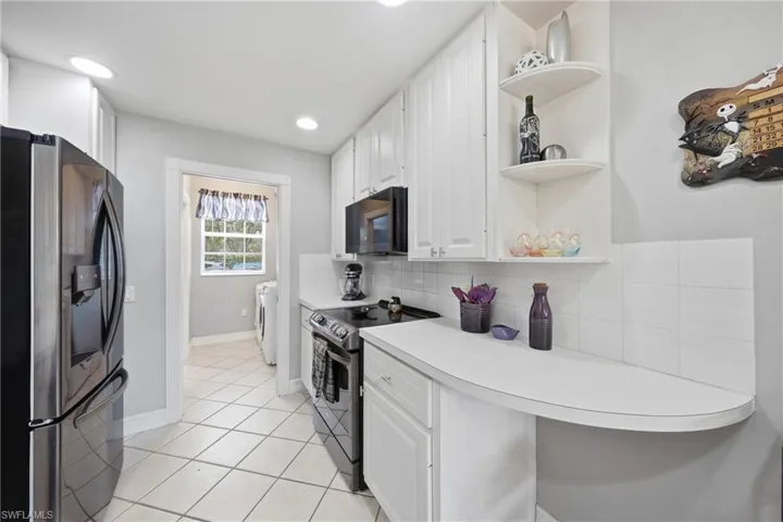 Galley kitchen featuring white cabinetry with brushed nickel hardware, a stainless steel refrigerator, and a black range