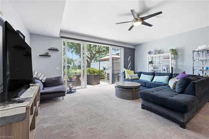 Living area featuring light gray wall paint, light gray carpet flooring, and a modern ceiling fan with integrated lighting