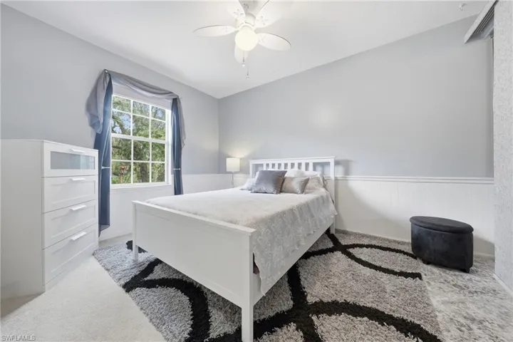Room featuring light gray walls with white wainscoting, a multi-pane window, and a ceiling fan with integrated lighting