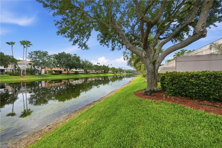 Waterfront property featuring a canal, mature trees, and manicured lawn