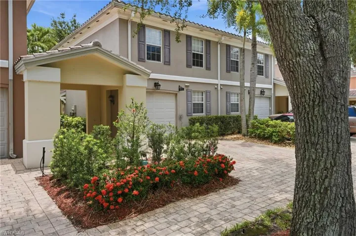 Two-story townhome featuring a covered entry, stucco exterior, gray window shutters, and an attached garage