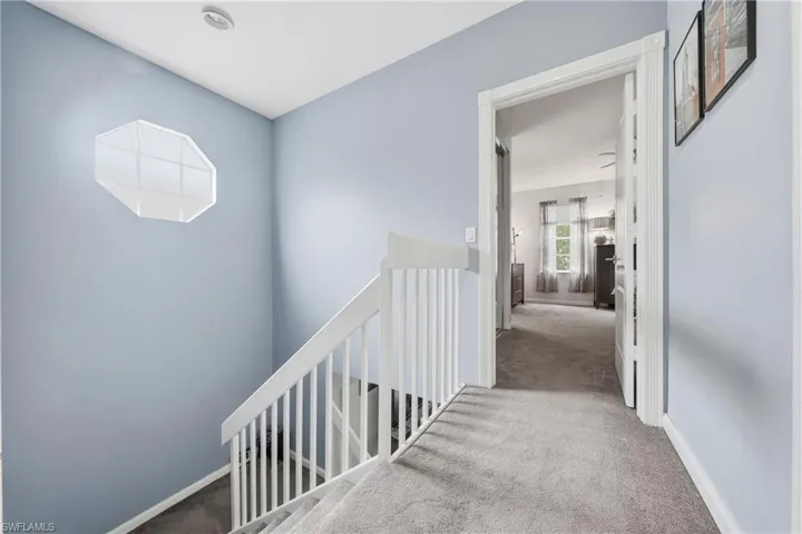 Carpeted staircase with white balusters and handrail, featuring a unique octagonal window and recessed lighting