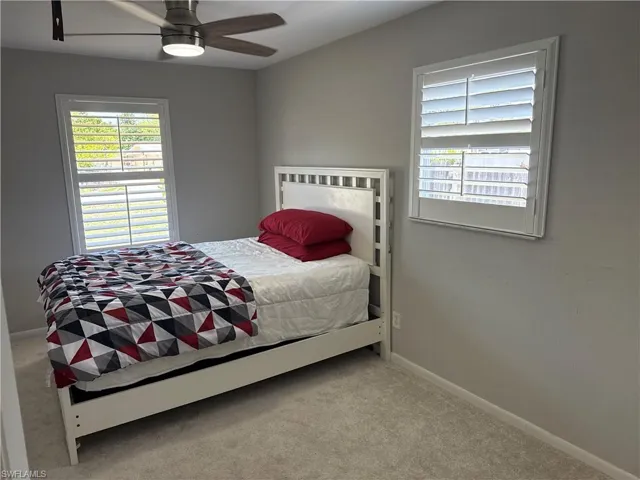 Carpeted bedroom with plantation shutters, ceiling fan, Queen Bed and 55" wall mounted flatscreen TV