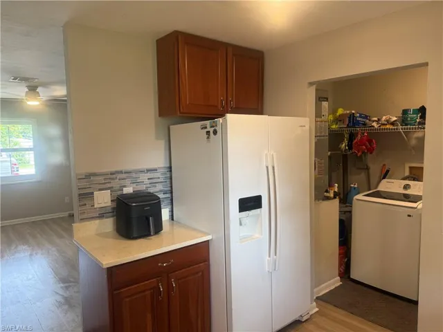 Kitchen featuring white refrigerator with ice dispenser, washer / dryer, light wood finished floors, backsplash, and brown cabinetry, utility room with new Samsung Washing machine.