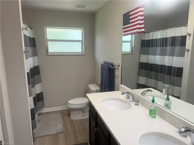 Full bathroom with plenty of natural light, wood finished floors, double vanity, and a shower with shower curtain