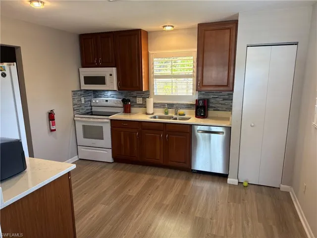 Kitchen with white appliances, light wood-style flooring, decorative backsplash, and light countertops