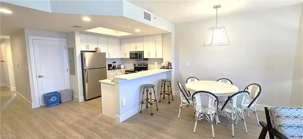 Kitchen featuring light hardwood / wood-style flooring, tasteful backsplash, kitchen peninsula, white cabinets, and stainless steel appliances