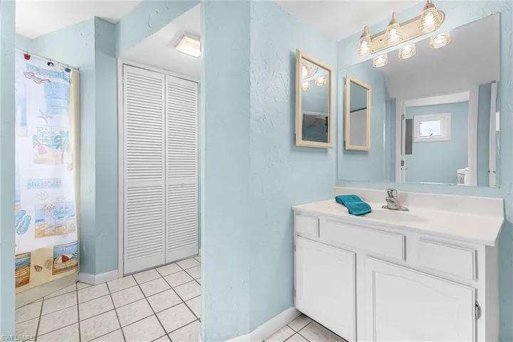 Full bathroom featuring a textured wall, vanity, a closet, light tile patterned floors, and a shower with shower curtain
