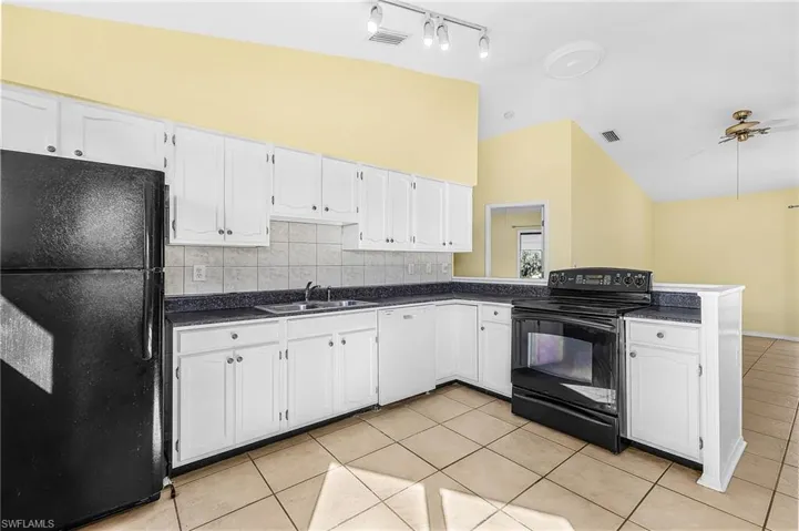 Kitchen featuring black appliances, dark countertops, white cabinets, lofted ceiling, and backsplash