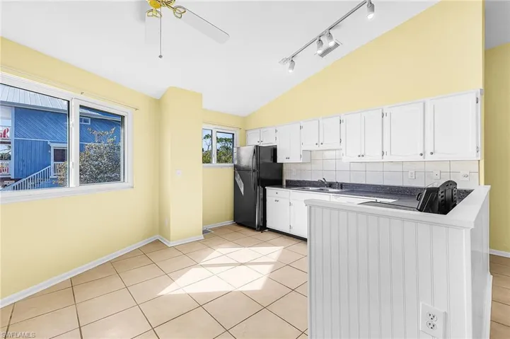 Kitchen featuring white cabinetry, vaulted ceiling, tasteful backsplash, freestanding refrigerator, and dark countertops