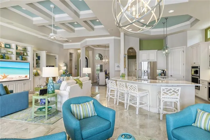 Living room featuring a towering ceiling, ornamental molding, coffered ceiling, ceiling fan with notable chandelier, and beamed ceiling