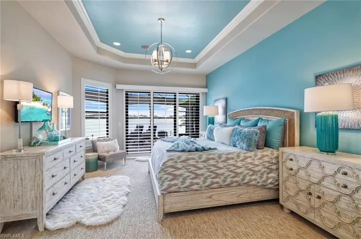Carpeted bedroom featuring a tray ceiling, an inviting chandelier, and ornamental molding