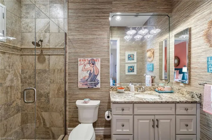 Bathroom with vanity, toilet, walk in shower, and tile walls