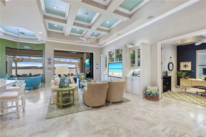 Living room with a high ceiling, coffered ceiling, crown molding, ceiling fan, and beamed ceiling