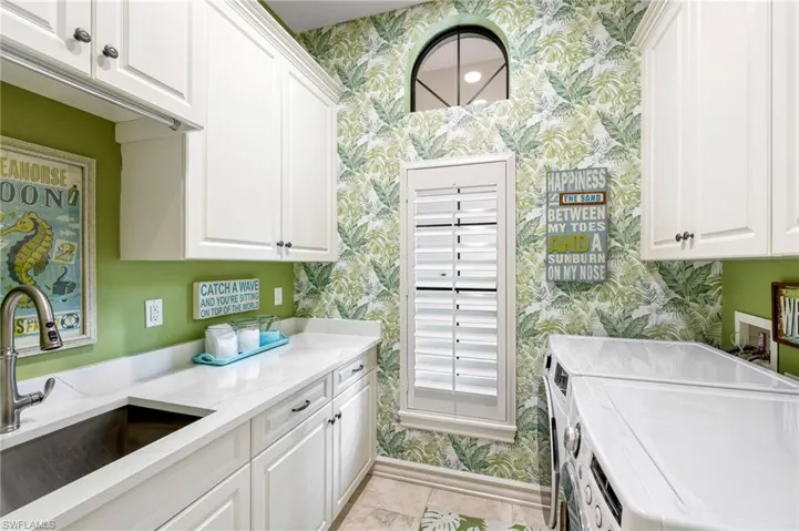 Laundry room featuring separate washer and dryer, sink, light tile patterned flooring, and cabinets