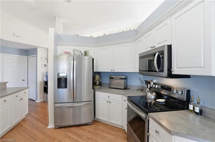 Kitchen featuring stainless steel appliances, white cabinetry, light wood finished floors, and light countertops