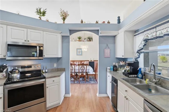 Kitchen with stainless steel appliances, white cabinetry, light wood finished floors, light countertops, and decorative light fixtures