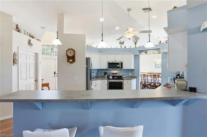 Kitchen featuring pendant lighting, stainless steel appliances, a ceiling fan, a kitchen bar, and dark countertops