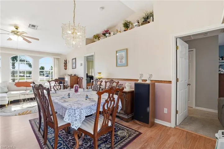 Dining space with vaulted ceiling, ceiling fan, light wood-style flooring, and a chandelier