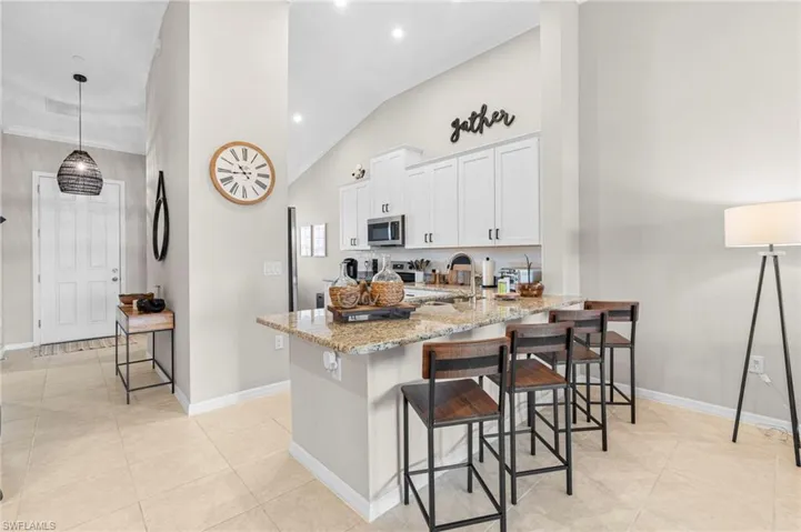 Kitchen with white cabinetry, light stone counters, a breakfast bar area, pendant lighting, and a peninsula