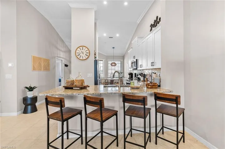 Kitchen with a breakfast bar area, light stone counters, white cabinetry, decorative light fixtures, and a peninsula
