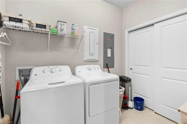 Washroom with electric panel, light tile patterned floors, and washer and dryer