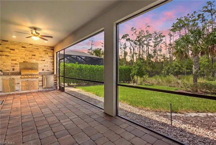 Screened lanai featuring paver flooring and an outdoor kitchen with built-in grill and stainless steel appliances