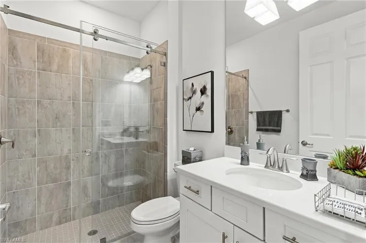 Built-in vanity with a white countertop and undermount sink, brushed nickel faucet, large mirror, and tiled shower with a glass enclosure