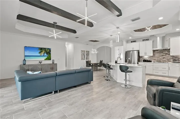 Spacious living area featuring coffered ceilings with wood beams, light wood-finish flooring, a kitchen island with seating, and stainless steel kitchen appliances