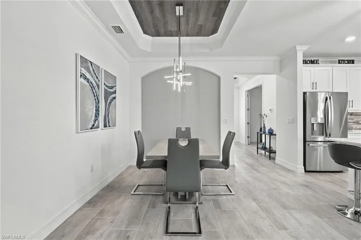 Recessed tray ceiling with wood-finish accent panel, plank-style flooring, arched doorway, and built-in stainless steel refrigerator