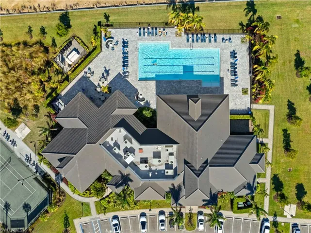 Community building with a dark gray tiled roof, an outdoor swimming pool, tennis court, and parking area