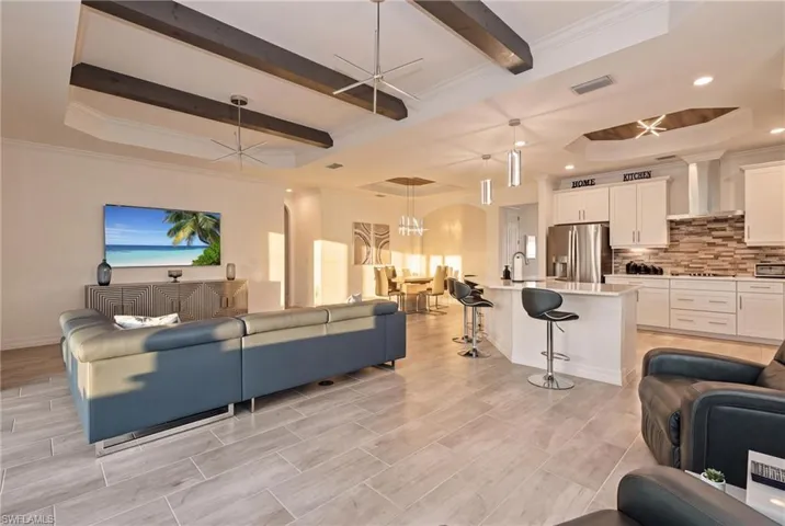 Open-concept living area with wood-finish tile flooring, a kitchen island with seating, stainless steel appliances, and a decorative tile backsplash