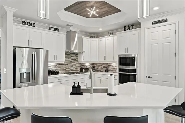 Kitchen featuring white shaker cabinetry, stainless steel appliances, a tile backsplash, and a multi-level island with a smooth countertop