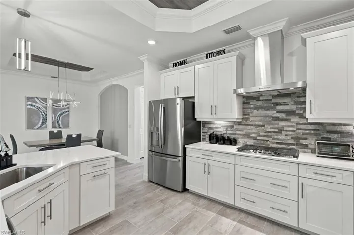 White shaker cabinetry, stainless steel appliances, tile flooring, stone tile backsplash, and a contemporary pendant light fixture
