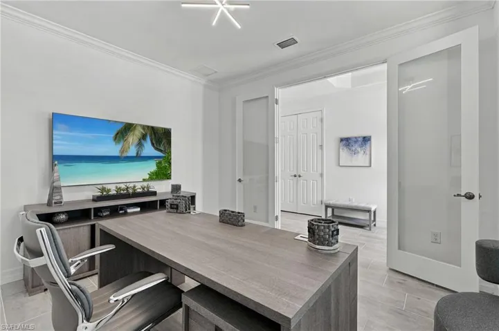 Bright room featuring crown molding, a built-in wood-finish desk, and large double French doors with frosted glass panels