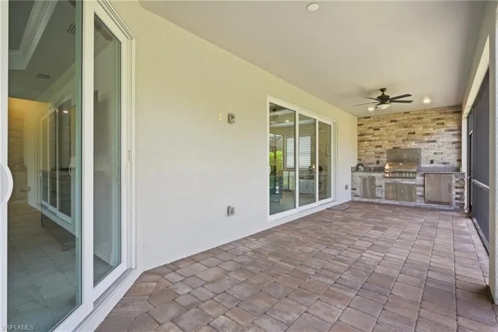 Covered patio featuring paver flooring, a built-in outdoor kitchen with stone veneer accents, and a ceiling fan