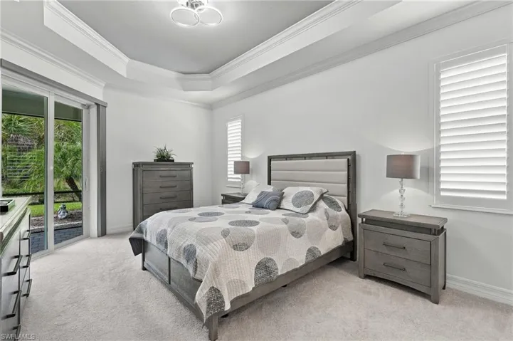 Recessed ceiling with crown molding, sliding glass door, plantation shutters, and light-colored carpeting