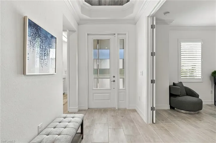 Recessed ceiling with layered crown molding, double-paned glass front door with sidelights, wood-finish tile flooring, interior plantation shutters