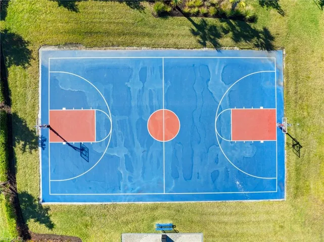 Basketball court featuring a blue playing surface, orange free throw lanes, white court lines, two basketball hoops, and surrounding green lawn