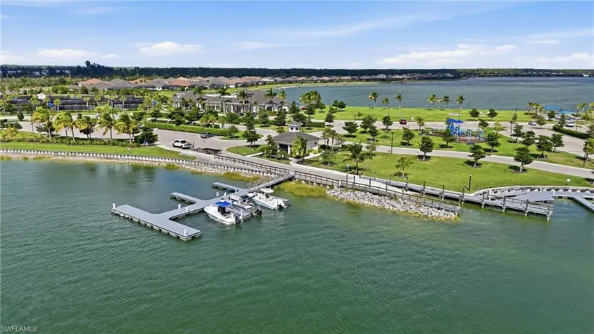 Waterfront property featuring a private boat dock, extensive green spaces, a community building, paved pathways, and mature palm trees